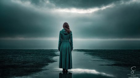 Frau in grünem Mantel vor dunklem Horizont